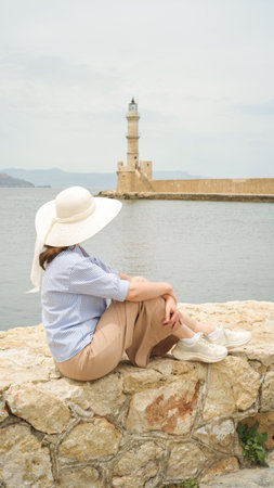 Woman wearing sun hat enjoying scenic view of the historic lighthouse in chania, crete, greeceの写真素材