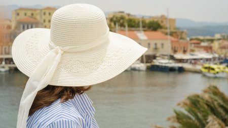 Woman wearing summer hat enjoying the view of boats and waterfront buildings in chania, creteの写真素材