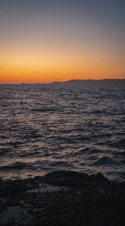 Tranquil ocean waves gently lapping against a rocky coastline beneath a breathtaking sunset skyの写真素材