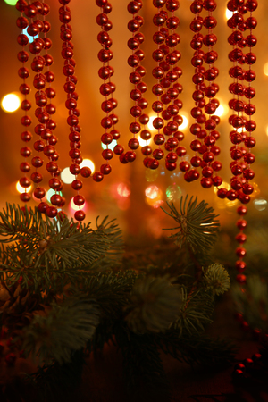 Beaded garlands decor. Red and orange christmas bokeh above firtree.  Abstract Christmas background.の写真素材