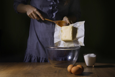 Women hands putting butter in bowl. Step of making cooking cake, preparing dough. Ingredients: butter, sugar, eggs.の写真素材