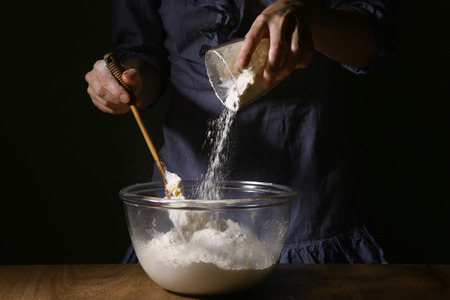 Women hands pouring flour in bowl. Step of making cooking cake, preparing dough.の写真素材