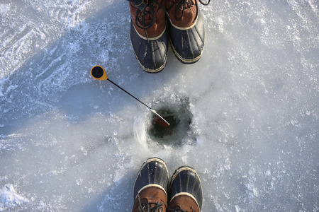Ice fishing on frozen lake. Two people  fishing together. Ice hole, winter rod and boots.の写真素材