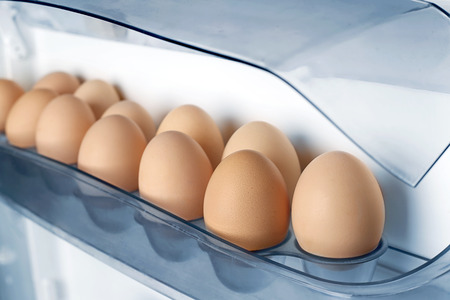 Eggs on fridge shelf. Chicken eggs on a shelf of the refrigerator door open closeup.の写真素材