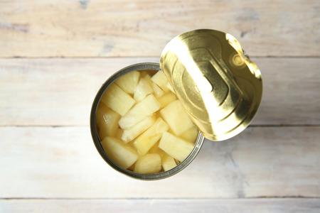 Opened tin can of canned pineapple pieces. Canned pineapple in can on wooden table top view.の写真素材
