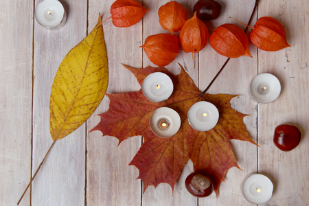 Autumn plant decorations and candles on wooden table. Leaves, chestnuts and chinese lantern and candles burning.の写真素材