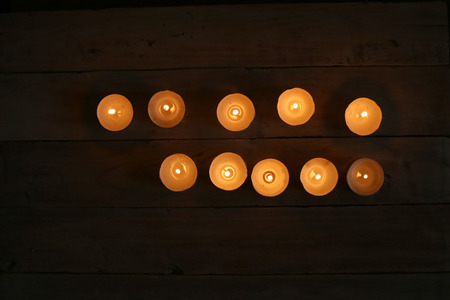 Burning candles  in the darkness. Small round tea light candles on wooden table top view.の写真素材