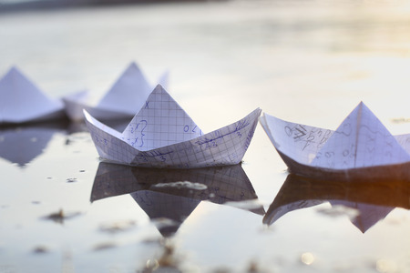 Origami paper ships sailing in river. Paper boats made from mathematics notebook paper.の写真素材