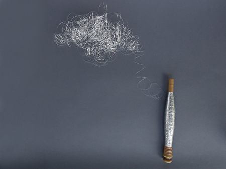 Silver thread pile like cloud and spool of silver thread. Reel or spool of silver thread on grey...