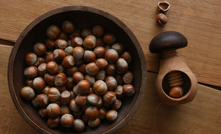 Wooden mushroom shape nutcracker and plate with hazelnuts, top view. Screw type nut cracker and...