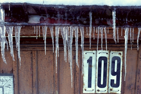 Icicles on old house roof. Vintage wooden wall with house number in winter time.の写真素材