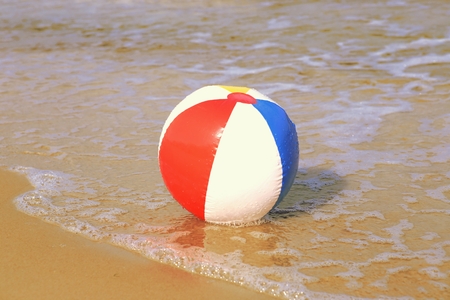 Ball on sand beach with wave. Holiday beach ball on sea wave.
