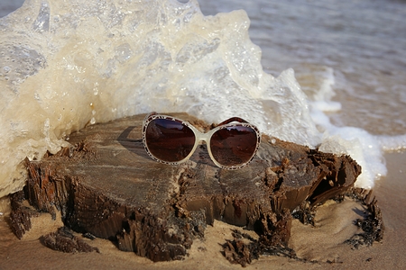 Sunglasses on a wooden stump on the sea beach. View of stump with sunglasses and sea wave.の写真素材