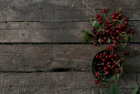 Freshly picked cherries in a bowl on a wooden table with empty place. Fresh ripe cherries harvested in bowl in summer garden. Top view.の写真素材