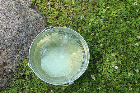 Metal bucket with fresh drink water. Top view. Zinc bucket with clear water on the grass outdoors.の写真素材