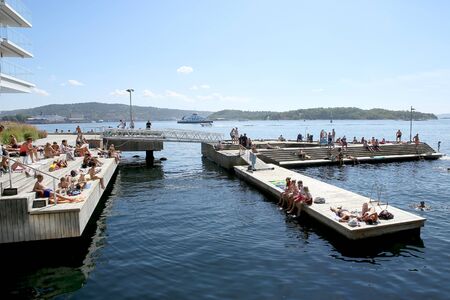 Oslo, Norway - July 24, 2018: Swimming beach in city center, Tjuvholmen neighborhood. Tjuvholmen city beach: people swimming,  relaxing in the summer sunshine on the boardwalk.のeditorial素材