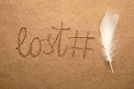 Word lost, hash tag and feather on sand background. Fun concept for internet or beauty theme.の写真素材