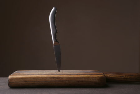 Knife stuck in cutting board on dark background. Wood cutting board with copy space.の写真素材