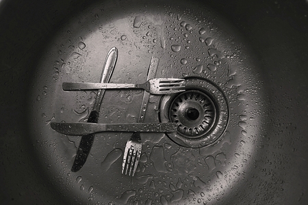 Forks with knifes as hashtag sign in kitchen sink. Close-up of water drops and plug hole.の写真素材
