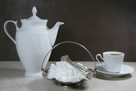 Sugar cubes in metal vintage sugar  bowl with sugar tongs and cups with coffee or tea pot.の写真素材