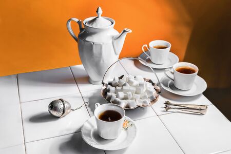 White tea cups and teapot, bowl with sugar cubes, tongs and tea stainer on white tiles table isolated on white background.
の写真素材