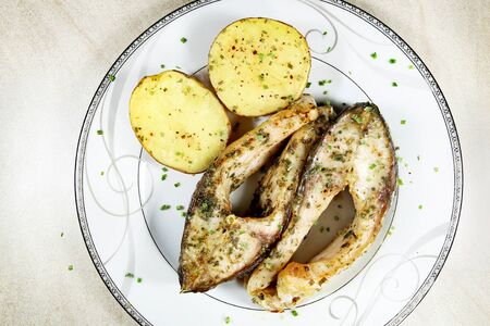 Pieces of baked carp with potatoes in plate. Dish of fish carp pieces and unpeeled potatoes baked in...