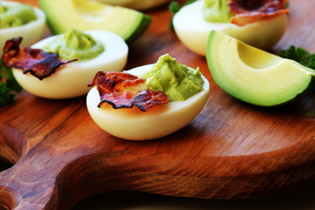 deviled eggs with avocado and bacon on cutting boardの写真素材