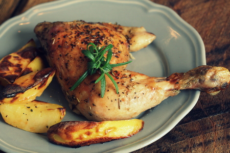 Grilled chicken quarter with potato for garnish. Top view. Wooden background