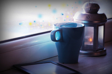 Winter decoration with lantern, hot tea cup,e-book reader and lights on windowの写真素材