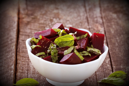 Beetroot chopped for salad with basil and dill seeds in bowl on rustic wooden tableの写真素材