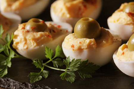 Spicy deviled eggs garnished with green olives on black background