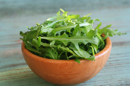 Fresh arugula leaves in wooden bowl, rucola on wooden old background .