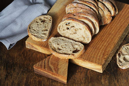 Freshly baked ciabatta bread sliced on wooden cutting board with knife .