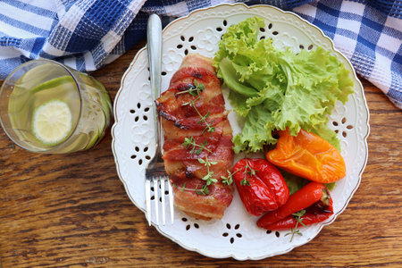 Dinner background. Grilled chicken breast wrapped in bacon served with salad on wooden rustic table . Top view .の写真素材