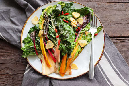 Wilted swiss chard salad with butter and garlic on rustic table .