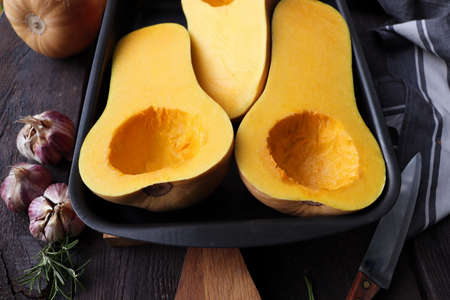 Halved butternut squash pumpkin on wood cutting board. Knife and kitchen towel on dark backgroundの写真素材