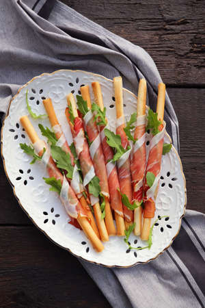 Antipasto platter cold meat plate with grissini bread sticks, prosciutto, slices ham, and arugula on...