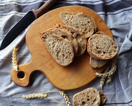 Freshly baked sliced rye bread on wooden cutting board with grains , flat lay