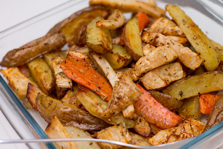 Oven baked potatoes and carrots in glass bowl with spoon on whiteの写真素材