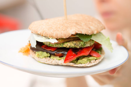 Girl holding elicious vegan burger on white plate in handの写真素材