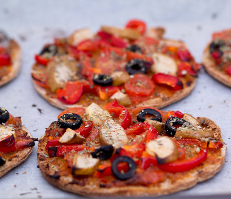 Home baked vegan mini pizza with olives, red pepper, tomato, pear, oregano and pesto on parchment...