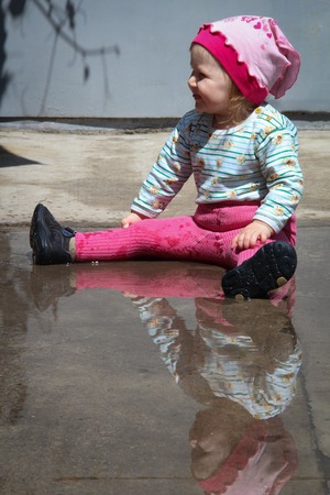 little funny girl playing with water in puddleの写真素材