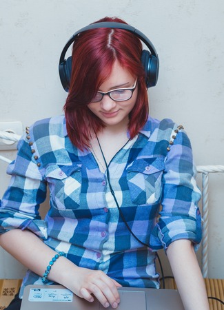 Beautiful young woman with Red Hair with headphones and laptop watching a movie on notebook in bed.の写真素材