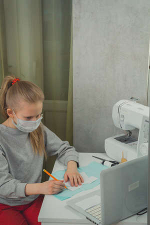 a girl is sitting at a table learning to sew a dress for a doll from video lessons at home