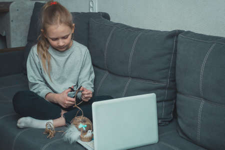 school girl sitting on sofa in living room and holding laptop in her lap, children internet addiction conceptの写真素材