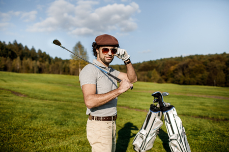 Full length view of man in cap holding golf club and hitting balの写真素材
