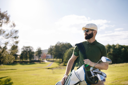 Golf player walking and carrying bag on course during summer gamの写真素材