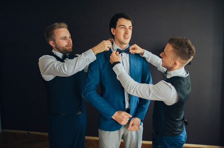stylish groomsmen helping happy groom getting ready in the morniの写真素材