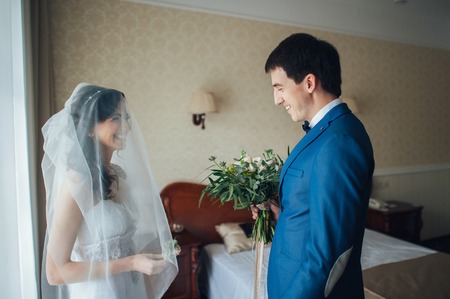 Bride and groom with a boutonniere stand in the roomの写真素材