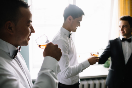 stylish groomsmen helping happy groom getting ready in the morningの写真素材